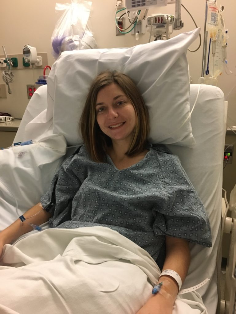 Young woman smiling in a hospital bed a few hours after having a Crohn's-related surgery