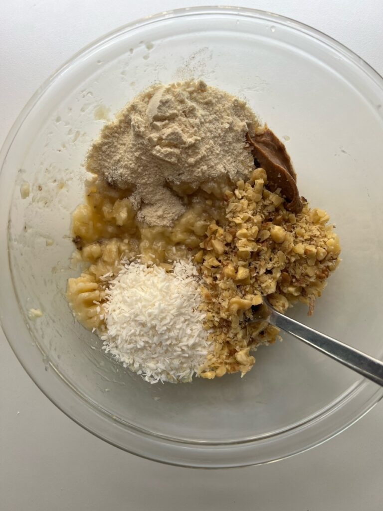 Bowl with banana, flour, almond butter, shredded coconut, and chopped walnuts